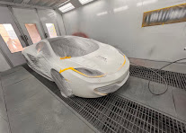 White sports car masked with yellow tape in the spray booth